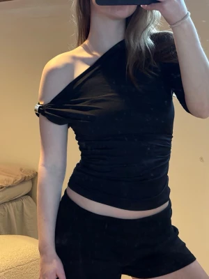 Oneshoulder topp - Snygg svart topp med oneshoulder-design och tight passform. Toppen är ärmlös på ena sidan och har en cool asymmetrisk look. Perfekt för dig som vill sticka ut med en trendig och stilren vibe. 🌸🩷🎀