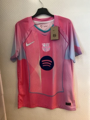 Barcelona matchtröja rosa Nike - Snygg Barcelona matchtröja i rosa och ljusblått från Nike med tryck av Lamine Yamal och nummer 10 på ryggen. Tröjan har klubbmärke, Nike-logga och Spotify-logga på bröstet. Tillverkad i lätt och ventilerande material, perfekt för fotboll eller träning. Jag fraktar i en nike påse