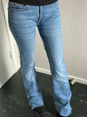 Ljusblå bootcut jeans med rå kant - Säljer ett par ljusblå bootcut jeans med råa kanter nertill och en liten slitning på bakfickan. Jeansen har klassisk femficksdesign och är tillverkade i stretchig denim för skön passform. Perfekta för en avslappnad och trendig look.