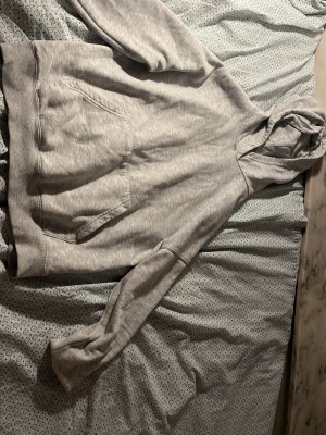 Ljusgrå basic hoodie med huva - En stilren ljusgrå hoodie med huva och stor magficka framtill. Klassisk modell med ribbade muddar vid ärmslut och nederkant. Perfekt för en avslappnad look. Materialet ser ut att vara mjuk bomullsblandning.