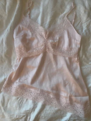 Ljusrosa spetsnattlinne  - Sött ljusrosa nattlinne från Gina Tricot i storlek XS. Tillverkat i ett mjukt, glansigt material med tunna axelband och spetsdetaljer vid byst och nederkant. Perfekt för mysiga kvällar hemma.