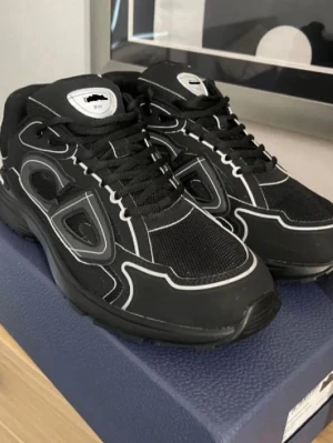 Svarta sneakers med vita detaljer - Snygga svarta sneakers med vita kontrastsömmar och detaljer. Skorna har en chunky sula och ovandel i mesh och syntetmaterial. Klassisk snörning och sportig design som passar till streetwear och casual outfits.
