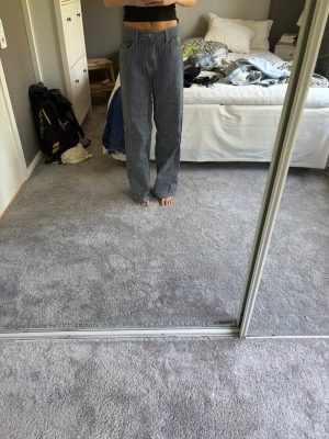 Blå raka jeans med hög midja - Säljer ett par blå vit randiga jeans med raka ben och mid waist midja. Jeansen har klassisk femficksdesign och är tillverkade i ett mjukt denimtyg. Passar perfekt till en avslappnad och trendig stil.