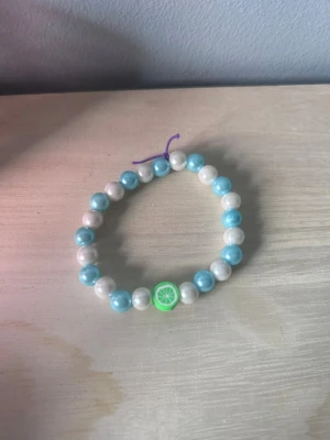 Två pärlarmband med pastellfärger - Säljer två söta armband med pärlor i pastellfärger. Det ena har vita och ljusblå pärlor samt en grön lime-detalj, det andra har skimrande pärlor i vitt och ljusblått. Perfekta accessoarer för att liva upp din stil.
