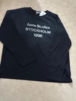 T-shirt manches longues Acne Studios 1996  - Brand new Acne Studios long-sleeve t-shirt in black, featuring the iconic 'Acne Studios STOCKHOLM 1996' white print on the front. Made from soft cotton, this tee includes stylish distressed details on the collar and hem, giving it a unique, worn-in aesthetic.   Condition : 10/10 (New with tags, in original packaging)  Size : L  Color : Black  Fast and careful shipping