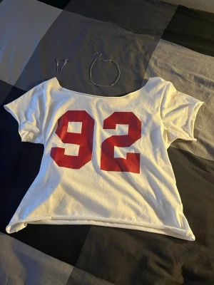 Vit offshoulder t-shirt med röd 92 - Säljer en vit offshoulder t-shirt med stort rött tryck av siffran 92 på framsidan. T-shirten har korta ärmar och en lös, avslappnad passform.