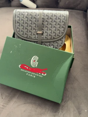 Grå mönstrad handväska med lock - Snygg grå handväska med klassiskt grafiskt mönster och lockstängning. Väskan har en elegant rem och detaljer i silver. Kommer i original grön låda. Perfekt för dig som gillar stilrena accessoarer med lyxig känsla.