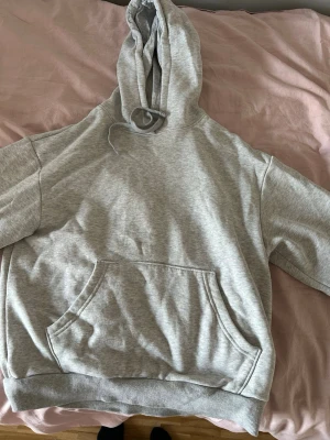 Ljusgrå hoodie med magficka - En basic ljusgrå hoodie med huva och dragsko. Hoodien har en stor magficka framtill och ribbade muddar vid ärmslut och nederkant. Tillverkad i mjukt sweatshirtmaterial som är perfekt för chill dagar.