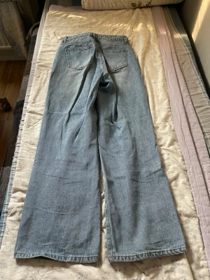 Ljusblåa raka jeans med hög midja - Säljer ett par ljusblå jeans med rak passform och hög midja som går att tjustera. Jeansen har klassiska fem fickor och breda ben, perfekta för en avslappnad och trendig look. Tillverkade i denim med en snygg tvättad finish.