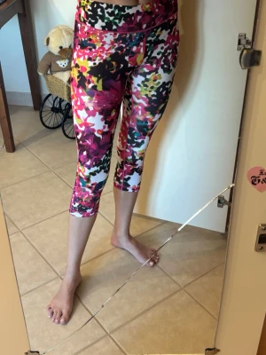 Färgglada mönstrade träningsleggings - Säljer ett par färgglada träningsleggings med blommigt och abstrakt mönster i rosa, vitt, svart, gult och grönt. Modellen är 3/4-längd och har bred midjeresår för extra komfort. Perfekta för gymmet eller yoga.