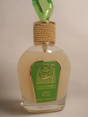 Musk Wild Vanille parfym - Unik parfymflaska från Thameen Collection med grön etikett och dekorativ grön kristallformad kork. Flaskan är genomskinlig med ljusgul vätska och har gulddetaljer runt halsen. Doften är Musk Wild Vanille, vilket ger en lyxig och exotisk känsla.