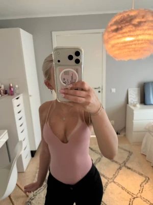 Ljusrosa body med tunna axelband - Säljer en ljusrosa body med djup urringning och tunna axelband. Bodyn har en enkel och stilren design som passar perfekt till olika outfits. Materialet ser ut att vara stretchigt och följsamt för en bekväm passform. Endast testad och lappen sitter kvar. ( skriv för fler bilder💕)