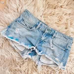 M12 Ljusblåa lågmidjade lowrise shorts med slitningar och färg splatter - Se fler shorts på min profil! Sååå snygga! Midja ca 37,5 cm rakt över