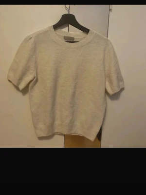 Beige stickad kortärmad topp - En ljusbeige stickad topp med korta ärmar och rund hals. Toppen har ribbade muddar vid ärmslut och nederkant samt en rak, normal passform. Perfekt för dig som gillar en enkel och stilren look.