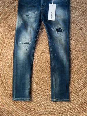 Blå slitna jeans från Dondup - Säljer ett par blå jeans från Dondup med skinny fit och slitna detaljer på benen. Jeansen har en tvättad look, hål och slitningar framtill samt klassiska bakfickor. Perfekta för en avslappnad och trendig stil. priset är ej hugget i sten