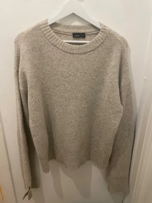 Beige stickad tröja från LMTD - Säljer en beige stickad tröja från LMTD i storlek M, passar ålder 15-16 år. Tröjan har rund halsringning, ribbstickade muddar och är gjord i mjukt material. Perfekt för lager på lager och enkel att matcha med jeans eller kjol. Använd fåtal gånger