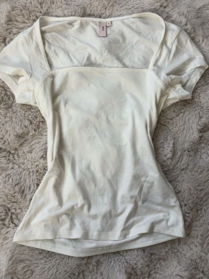 Vit topp med fyrkantig ringning Nelly - Säljer en vit topp från Nelly med korta ärmar och snygg fyrkantig ringning. Modellen är figurnära och har en enkel, stilren design som passar till allt. Tillverkad i mjukt bomullsmaterial för skön känsla hela dagen.