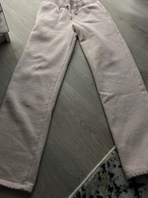 Ljusrosa mjukisbyxor med dragsko - Säljer ett par ljusrosa mjukisbyxor med raka ben och bred resår i midjan samt dragsko. Byxorna är tillverkade i ett mjukt och skönt material, perfekta för chill dagar. Inga synliga loggor eller märken. Passar dig som gillar en relaxed och enkel stil. Färgen har dock färgat av sig .