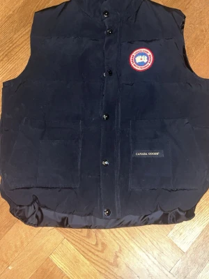 Canada goose väst - Säljer en svart dunväst från Canada Goose med klassisk logga på bröstet och två stora fickor framtill. Västen har hög krage, knäppning med knappar och är fylld med dun för extra värme. Perfekt för lager-på-lager och streetwear-stil. Passar perfekt nu till våren när det börjar bli varmare. Pris kan diskuteras. Finns en gucciväska också men kan inte lägga upp den, kom pv för frågor och intresse om den. 