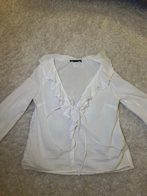 Vit volangblus från 157 XS - Söt vit blus från 157 i storlek XS med långa ärmar och volangkant längs den djupa v-ringningen. Blusen har knytband framtill. Aldrig använd 