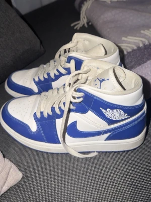 Air Jordan 1 Mid blå och vita sneakers - Säljer ett par Air Jordan 1 Mid sneakers i blått och vitt. Storlek US 8,5 (passar 38-39 skulle jag säga) superbra skick, knappt använda och finns inte längre att köpa 😍