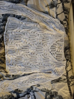 Vit virkad stickad tröja med mönster - Säljer en vit stickad tröja med virkat mönster och v-ringning. Tröjan har långa ärmar och är tillverkad i ett luftigt material som ger en avslappnad och trendig look. Perfekt att slänga på sig över ett linne eller topp. 