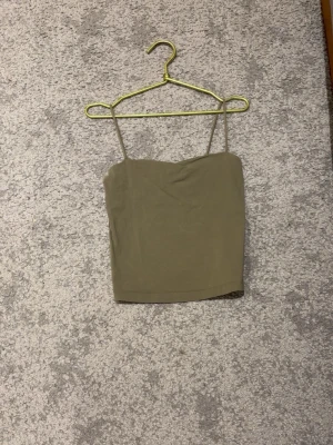 Grön linnetopp med smala axelband - Snygg grön linnetopp med smala axelband och rak skärning. Perfekt till jeans eller kjol för en enkel och stilren look. Tunn och lätt, passar bra till varma dagar.