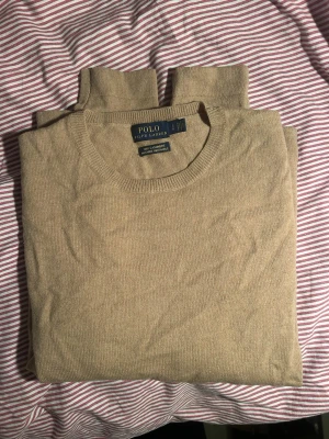 Brun stickad tröja från Ralph Lauren - Super söt tröja från Ralph Lauren i storlek S! Jätte bra skick. Brun/ beige färg, mest lik verkligheten på bild 3. Har en polohäst i samma färg som tröjan och slitningar längst ner💕💕