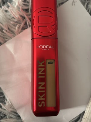 L'Oréal Skin Ink Foundation röd - Läppstift från L'Oréal Paris i serien Skin Ink. Kommer i en snygg röd plastförpackning med guldfärgad text och genomskinligt fönster som visar produktens nyans. Modern och kompakt design som är enkel att ta med sig.