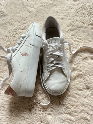Vita sneakers från Polo Ralph Lauren - Snygga vita sneakers från Polo Ralph Lauren med rosa logga på sidan. Jätte fint skick sparsamt använda!! Kom privat för mer bilder🥰