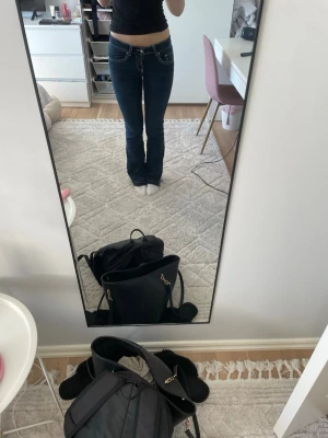 Mörkblå bootcut jeans med kontrastsömmar - Säljer ett par mörkblå bootcut jeans med snygga kontrastsömmar och klassisk femficksdesign. Jeansen har låg midja och är tillverkade i stretchigt denimtyg för skön passform. Perfekta till en avslappnad look och passar till det mesta i garderoben. Har sprättat upp dem nere för att få dem i rätt längd (är 175)