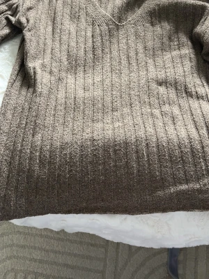 Brun ribbstickad tröja med v-ringning - Säljer en brun ribbstickad tröja med v-ringad hals och långa ärmar. Tröjan har en avslappnad passform och är tillverkad i ett mjukt, värmande material som passar perfekt för kyligare dagar. Klassisk och enkel design som är lätt att matcha.