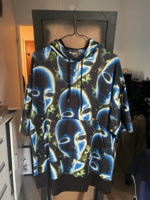 ASOS oversized hoodie med alienmönster - Cool oversized hoodie från ASOS i storlek XS med unikt blått och svart alienmönster. Hoodien har huva med svarta snören och en stor magficka. Materialet är mjukt och bekvämt, perfekt för dig som vill sticka ut med din stil.