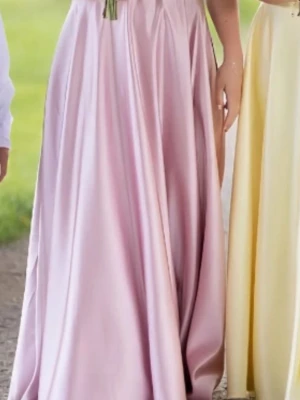 Ljusrosa långklänning i satin - Elegant ljusrosa långklänning i glansigt satinliknande material. Klänningen har en hög midja och ett svepande, utsvängt kjolparti som ger en klassisk siluett. Perfekt för bal eller student.                                                       Orginalpåse finns!!                                                        Ligger på flera sidor. 