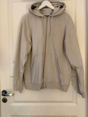 Beige zip-hoodie från Weekday - Säljer en beige hoodie med dragkedja från Weekday. Hoodien har huva med dragsko, två fickor framtill och ribbade muddar vid ärmslut och nederkant. Perfekt oversized passform och tillverkad i mjuk bomullsblandning.