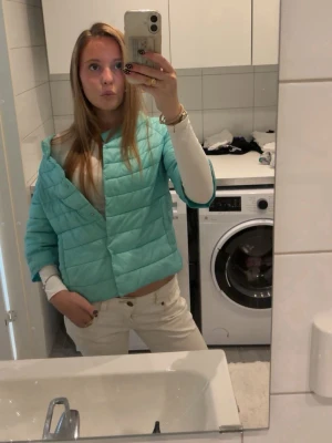 Turkos trekvartsjacka från Monte Cervino - Säljer en turkos pufferjacka från Monte Cervino med trekvartsärmar och boxig passform. Jackan har diskreta sömmar och knappfickor på sidorna. Perfekt för att sticka ut i vårvädret med en cool och modern look.