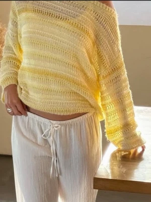 Gul stickad tröja - Säljer en ljusgul, transparent stickad tröja med avslappnad passform och bred halsringning. Tröjan har ett luftigt, hålmönstrat material och långa ärmar. Perfekt för lager på lager och ger en fräsch sommarkänsla.