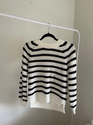 Vit och svart randig stickad tröja - Säljer en snygg stickad tröja med breda svarta och vita ränder. Tröjan har rund halsringning, långa ärmar och ribbade muddar vid ärmslut och nederkant. Perfekt för dig som gillar klassisk och enkel stil. 