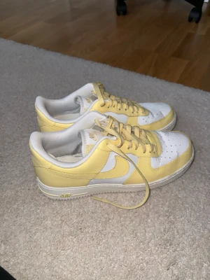 Nike Air Force 1 Low vit/gul - Säljer ett par Nike Air Force 1 Low sneakers i vitt och ljusgult läder. Använd ca 4 gånger. 
