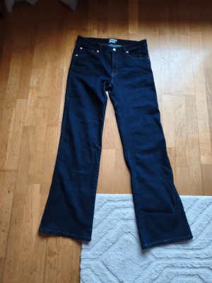 Mörkblå bootcut jeans - Snygga mörkblå bootcut jeans med klassisk femficksdesign och silverfärgade nitar. Jeansen har hög midja och vida ben, perfekta för en trendig och avslappnad stil. Tillverkade i denim med en stilren look.