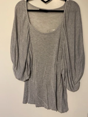 Grå topp med vida ärmar - Snygg grå topp med rund halsringning och riktigt vida, puffiga ärmar som ger en unik look. Tillverkad i mjukt material som känns skönt mot huden. Perfekt för dig som vill ha något enkelt men ändå speciellt.