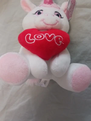 Mjukisdjur enhörning med hjärta - Söt vit och rosa mjukisenhörning i plysch som håller ett rött hjärta med texten 'LOVE' broderat i vitt. Enhörningen har stora ögon, rosa detaljer och ett glittrigt horn. Perfekt som present eller dekoration.