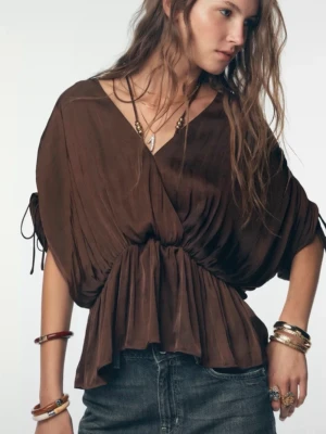 Brun omlottopp från Zara - Snygg brun omlottopp från Zara i storlek s med v-ringning och volang nertill. Toppen har korta ärmar med rynkade detaljer och knyt i sidorna. Tillverkad i ett glansigt, mjukt material som ger en lyxig känsla. Aldrig använd lappen sitter fortfarande kvar😊