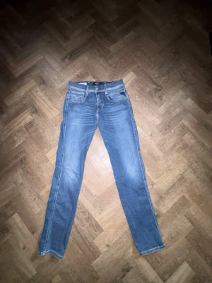 Blå jeans från Replay - Klassiska blå jeans från Replay med raka ben och femficksdesign. Jeansen har ljusa slitningar och tydliga sömmar, samt en liten logotyp på bakfickan. Perfekta för en avslappnad och stilren look. Size: 28. Mer jeans finns på min profil 