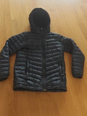 Svart vår / höst dunjacka från Peak Performance. - En svart dun jacka för höst och vår väder. Från Peak Performance i storlek 150. Den är i perfekt skick förutom en liten skadda på luvan som man kan se i bild 3. Annars så är den i som ny skick. Skriv gärna om du är intresserad och har frågor.