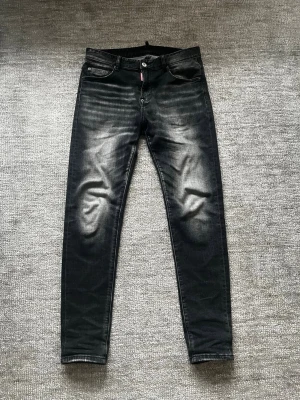Svarta Dsquared2 jeans med slitningar - Svarta Dsquared2 slim fit jeans med slitningar och tvättade detaljer på framsidan. Klassisk femficksmodell med knapp och dragkedja. Perfekta för en trendig och avslappnad stil.