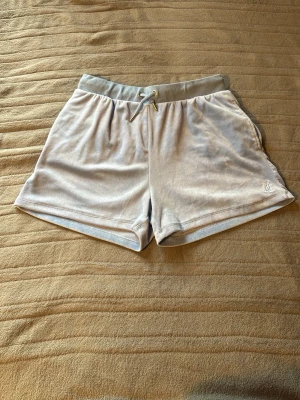 Ljusgrå shorts med snörning - Säljer ett par ljusgrå velourshorts från Juicy Couture med snörning i midjan och fickor på sidorna. Shortsen passar både XS och S. Och är bara använda några gånger.