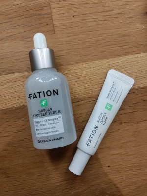 Fation Nosca9 Trouble Serum set - Fation Nosca9 Trouble Serum och tillhörande kräm, perfekt för känslig hud. Serumet kommer i en genomskinlig glasflaska med pipett och silvrigt lock, medan krämen är i en vit tub. Båda är dermatologiskt testade och utvecklade för att lugna huden.