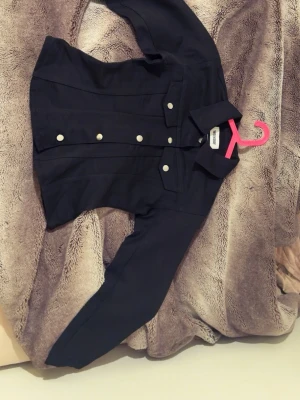 Figursydd jeansjacka - Snygg svart jeansjacka med raka linjer och klassisk krage. Jackan har två bröstfickor med lock och silverfärgade knappar framtill. Perfekt att slänga över en hoodie eller t-shirt för en cool och enkel look.