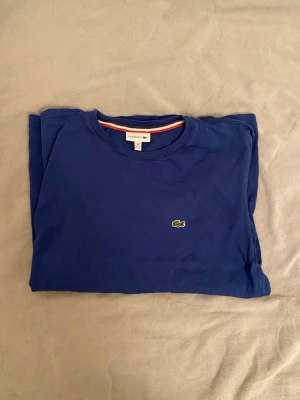Lacost T-shirt - Snygg blå t-shirt från Lacoste med klassisk krokodillogga på bröstet. T-shirten är i toppen skick men lite skrynklig på bilden bara. Priset är inte hugget i sten och bara hör av er vid minsta fråga🫡